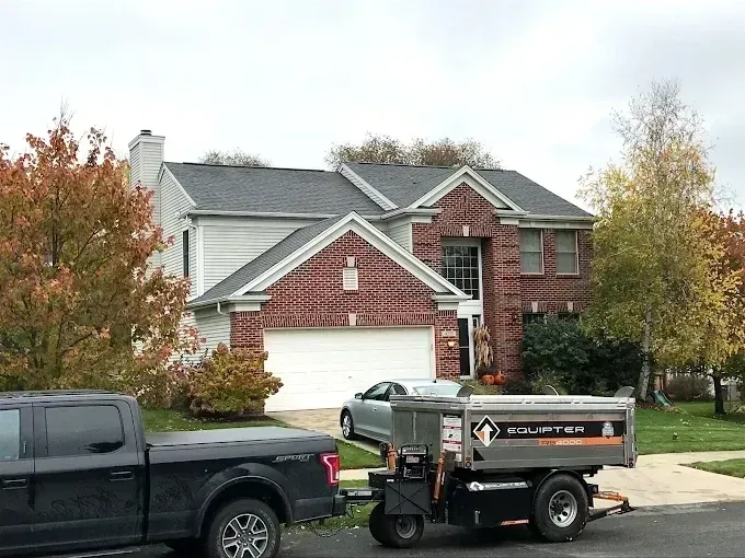 Suburban brick house with white garage, black pickup truck and utility trailer parked in the driveway.