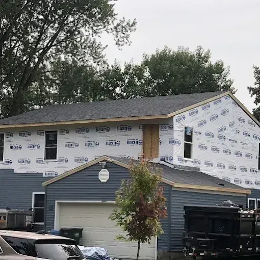House under construction with white wrap and blue siding, seen behind a truck in a residential driveway