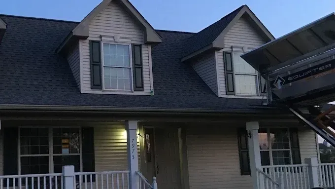Suburban house with dormer windows, front porch, and attached garage at dusk
