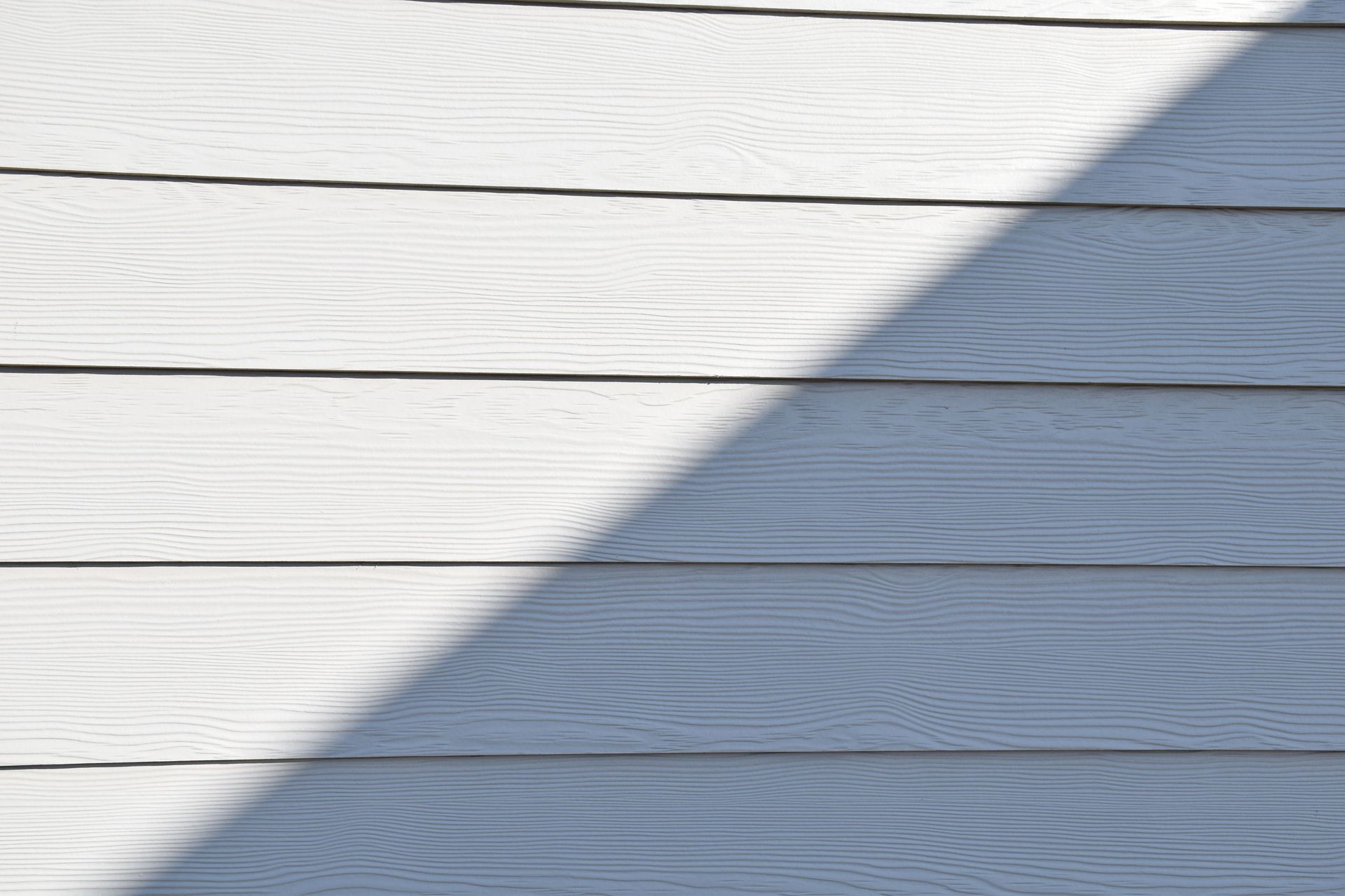 White wooden siding with horizontal boards, partly covered by a diagonal shadow.