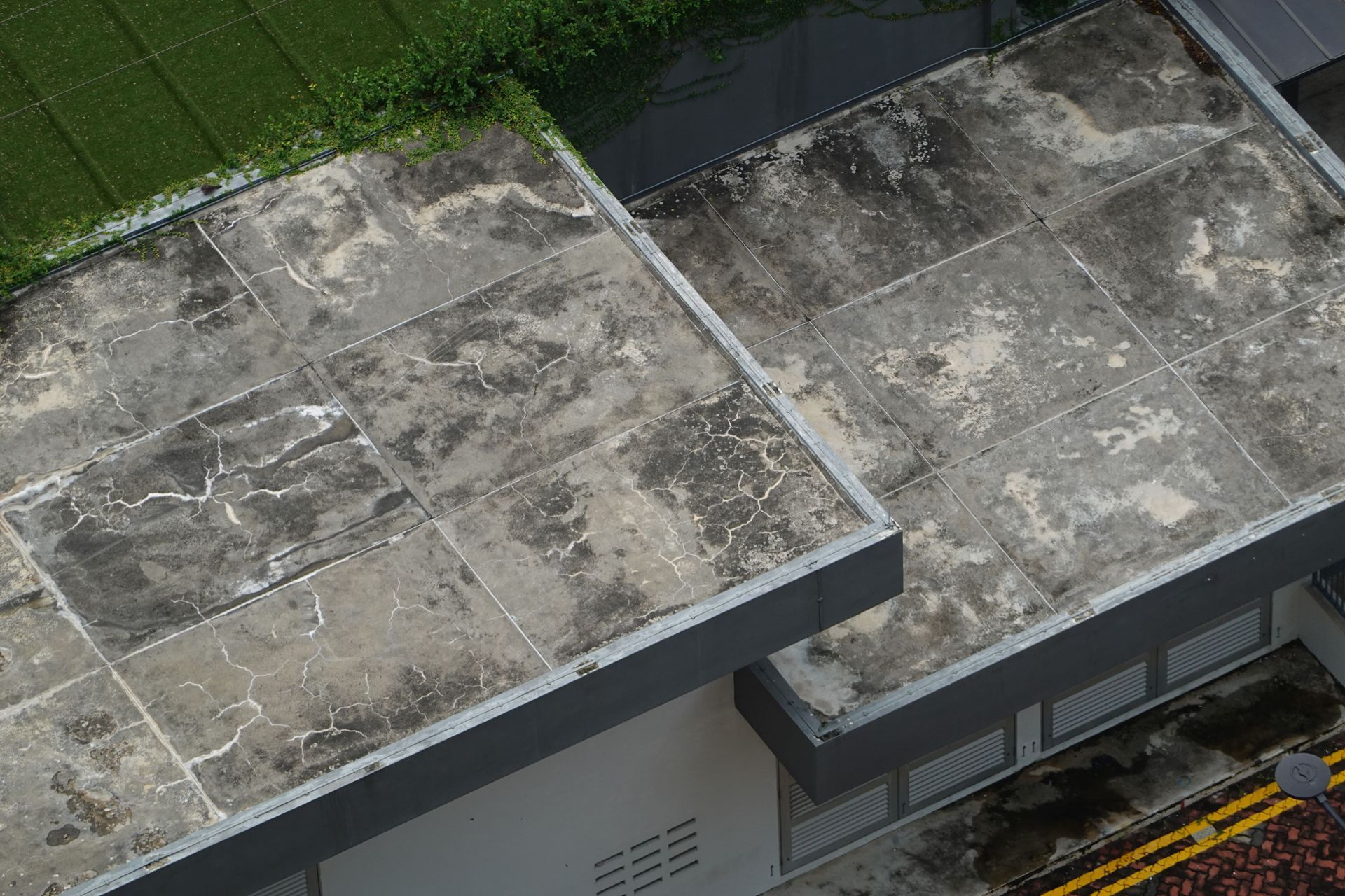 Overhead view of a flat, weathered rooftop beside a strip of green grass.