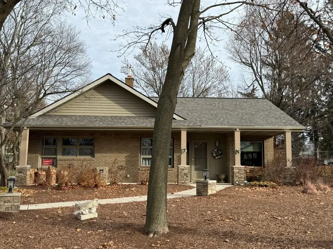Single-story brick house with a front porch and a large tree in a leaf-covered yard.