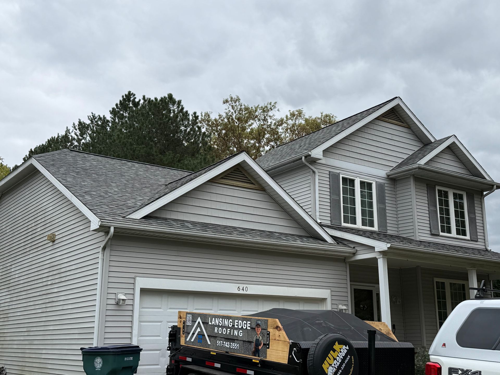 Gray suburban house with a white garage, parked white SUV, and construction dumpster in the driveway