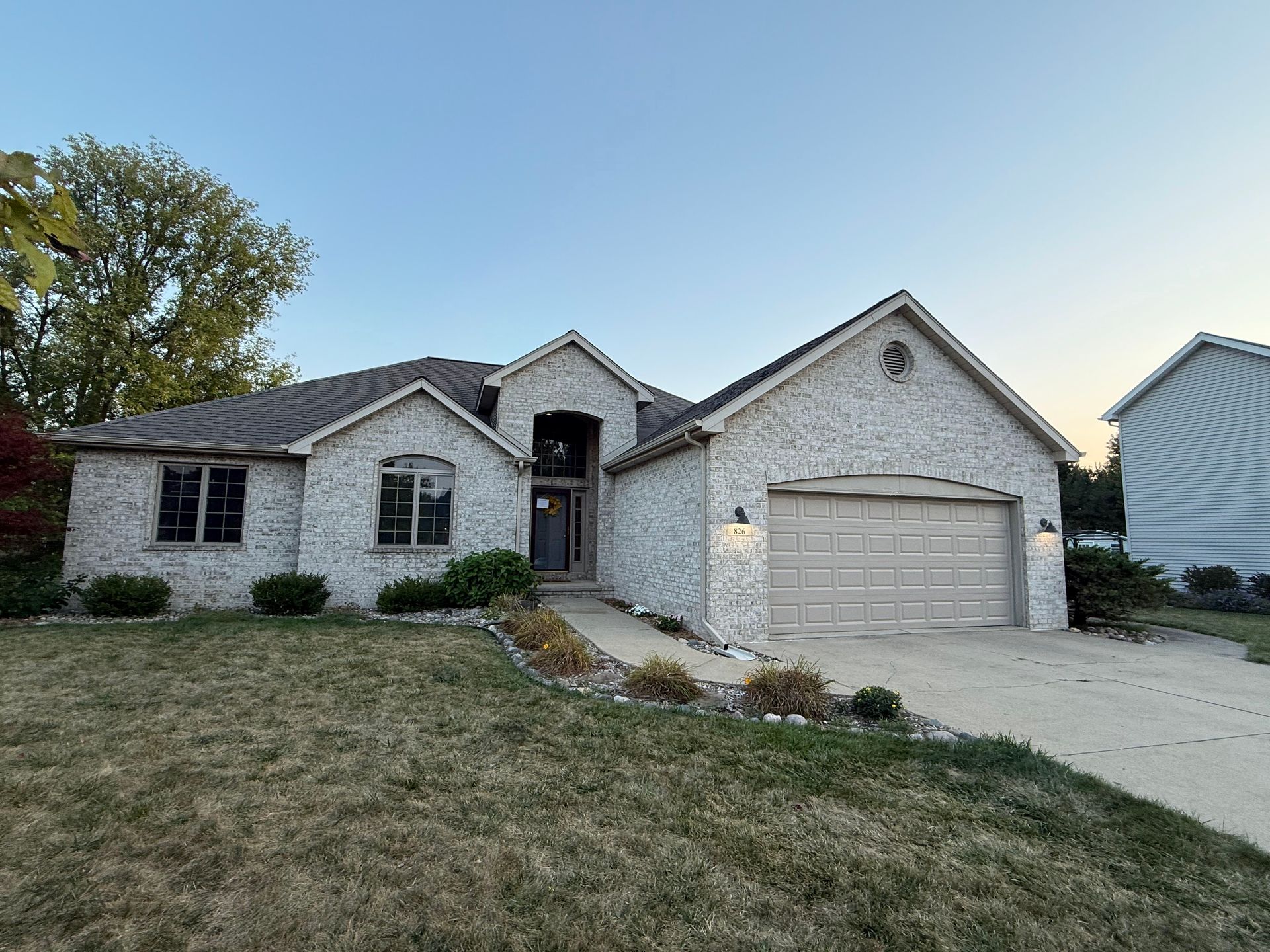 Single-story brick house with two-car garage and a sloped front lawn at dusk