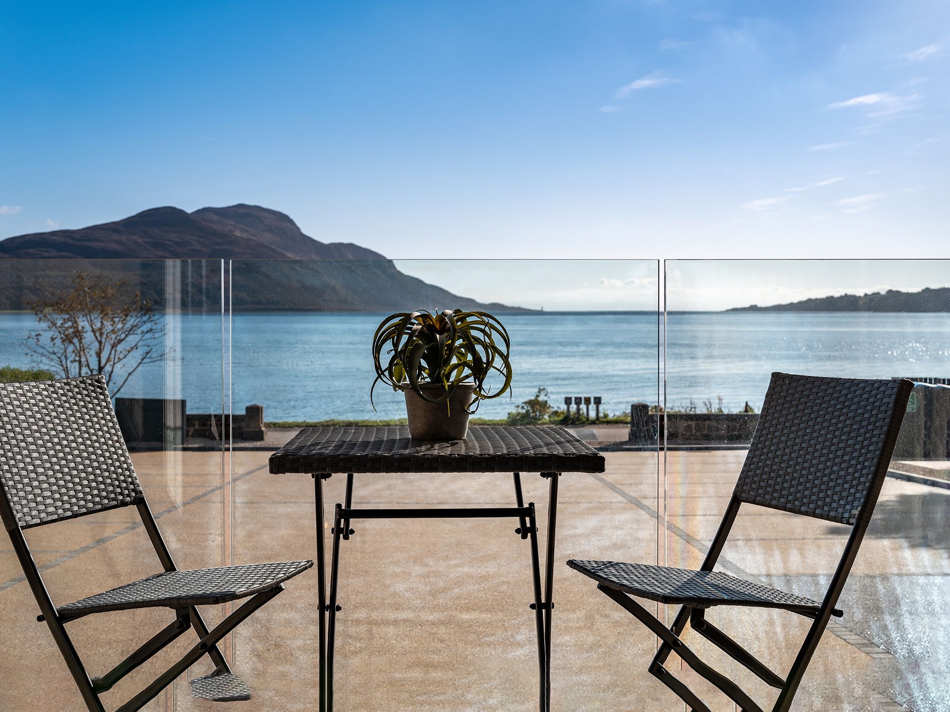 A table and chairs on a balcony overlooking the ocean.