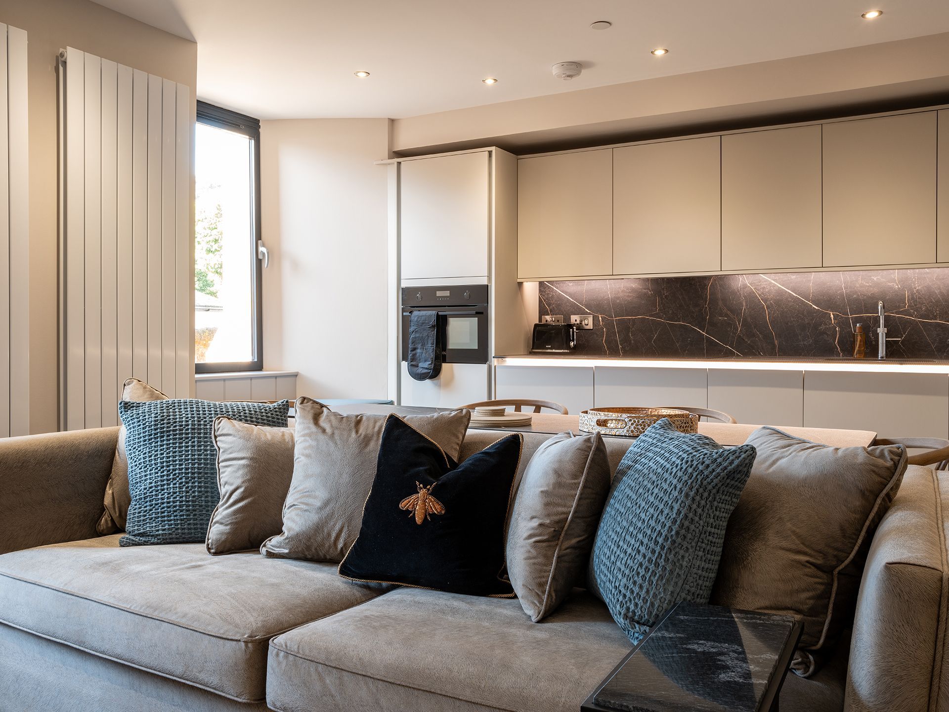 A living room with a couch and pillows and a kitchen in the background.