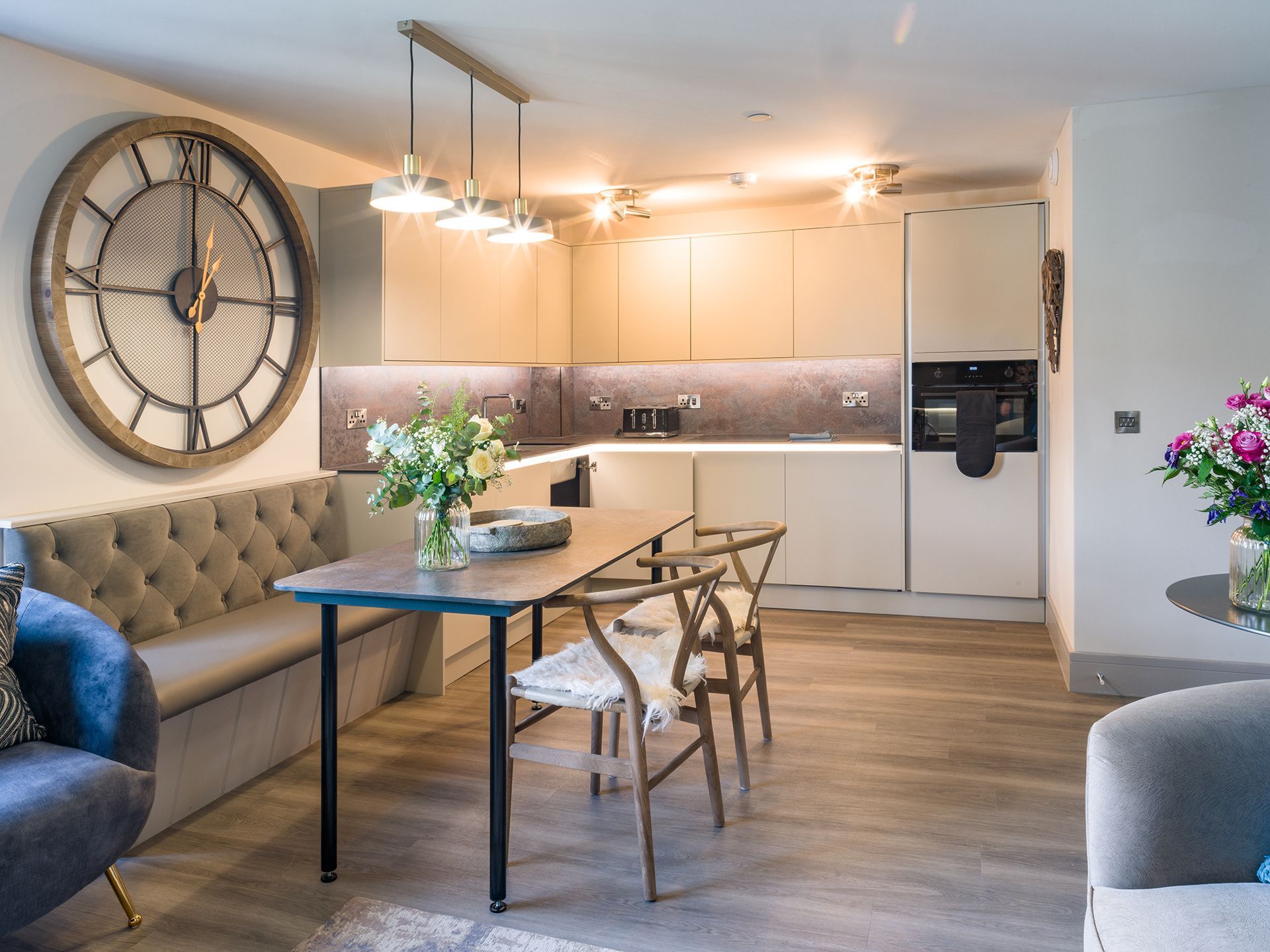 A kitchen with a table and chairs and a large clock on the wall.