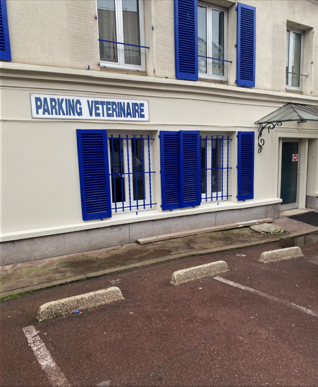 Un bâtiment blanc avec des volets bleus et un panneau indiquant parking vétérinaire