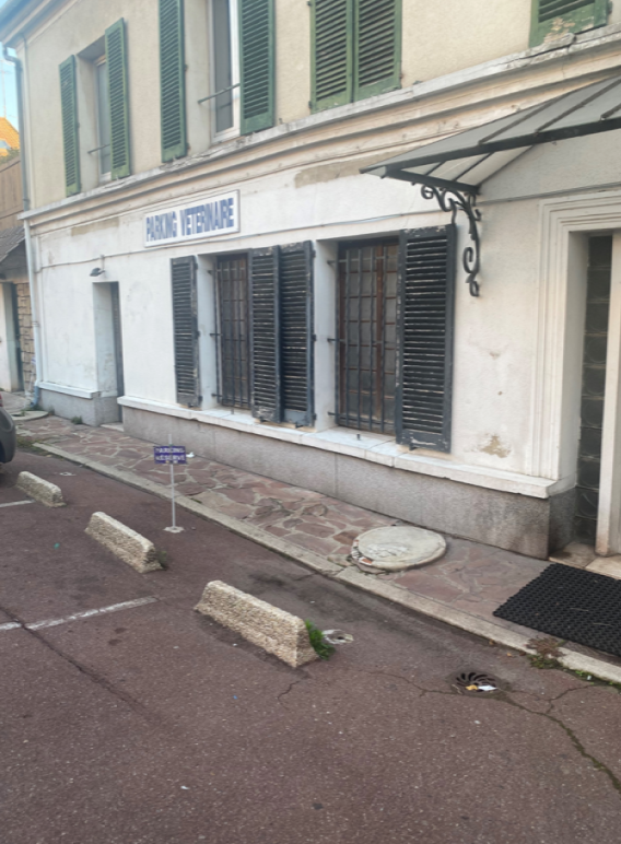 Un immeuble avec des volets aux fenêtres et un parking devant.