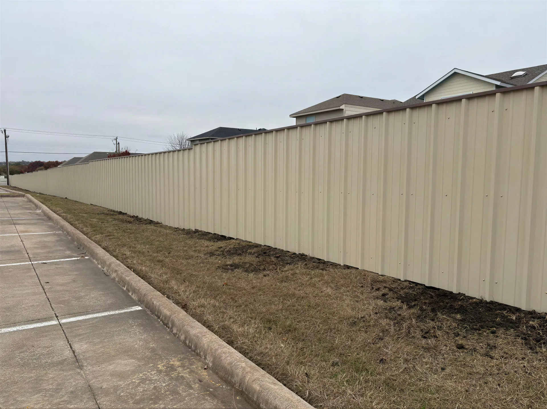 Long beige fence along a roadside beside a gravel strip under a cloudy sky