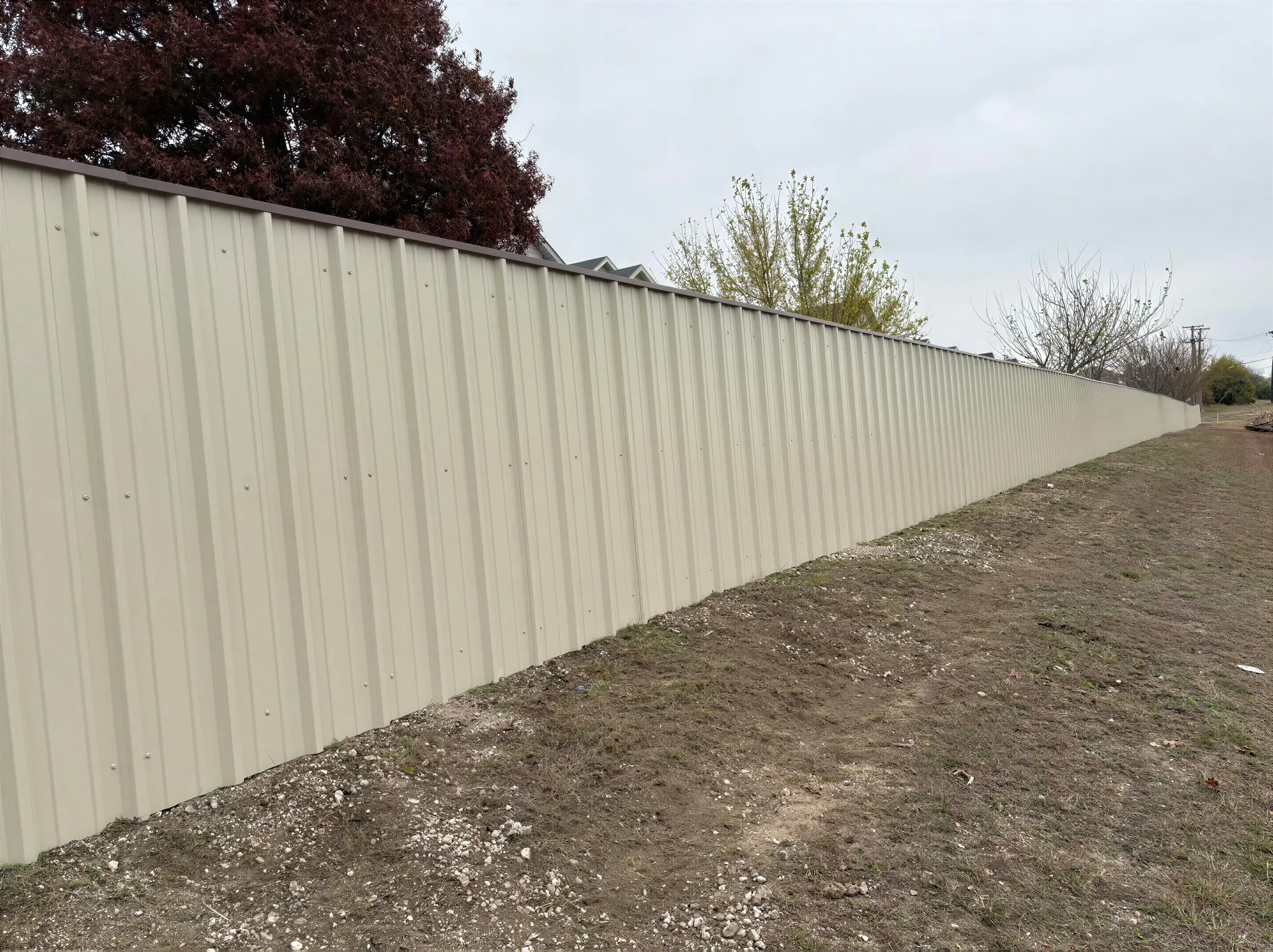 Long beige metal fence beside a gravel embankment under an overcast sky