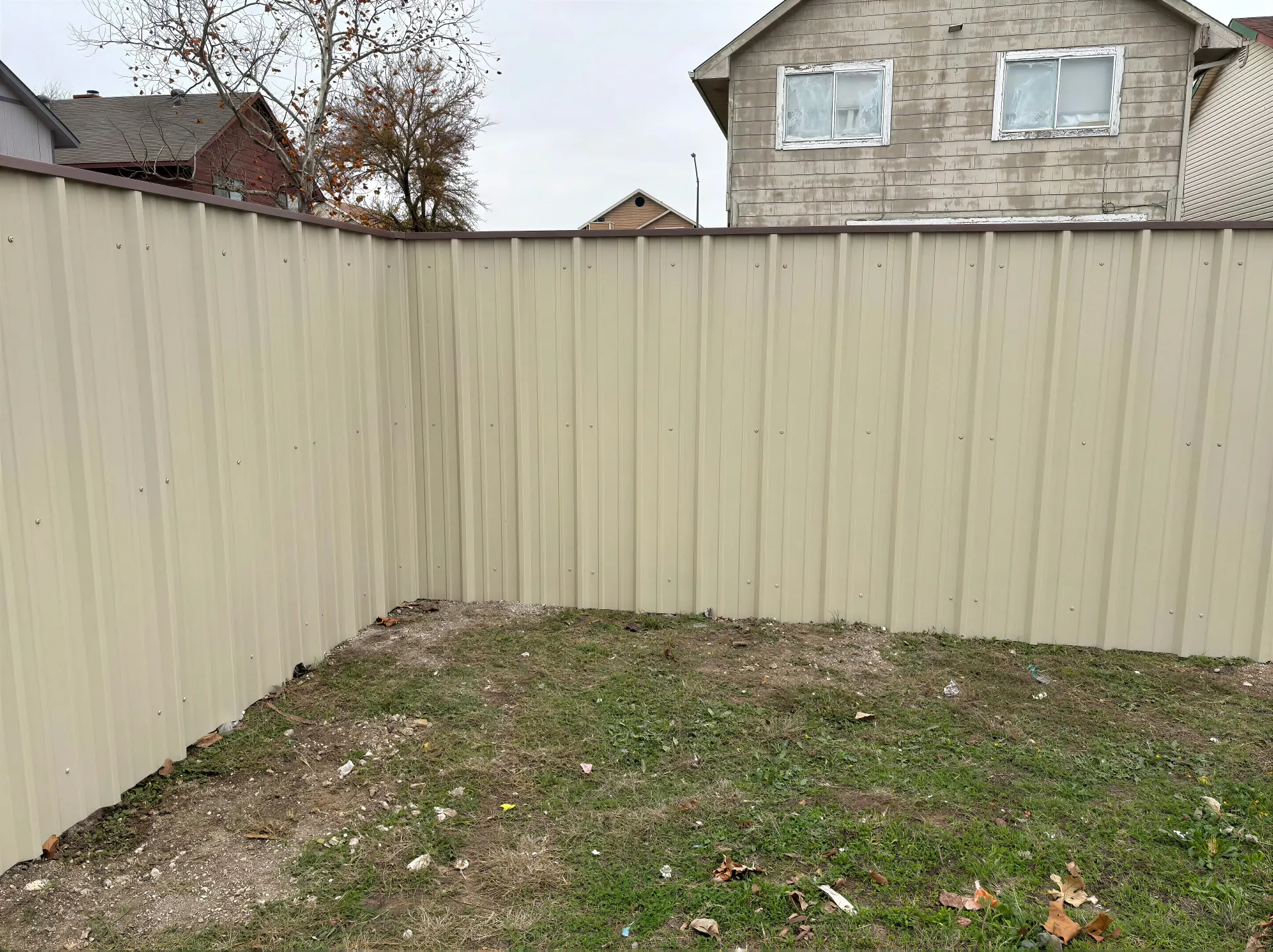 Small fenced backyard with beige wooden privacy fences and sparse grass.