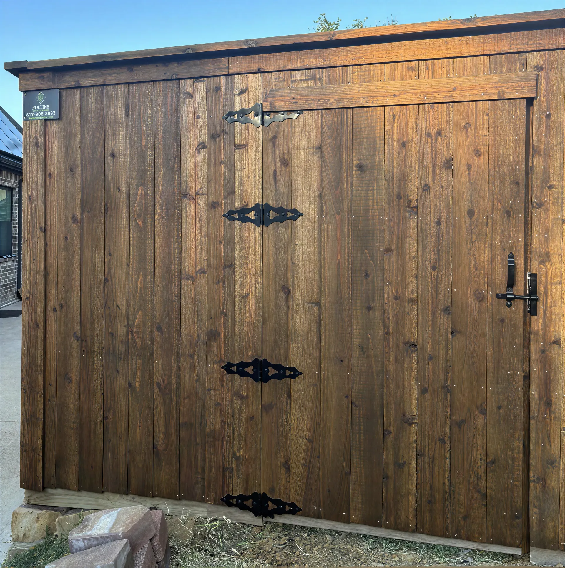 Weathered wooden shed door with black hinges and latch in sunlight