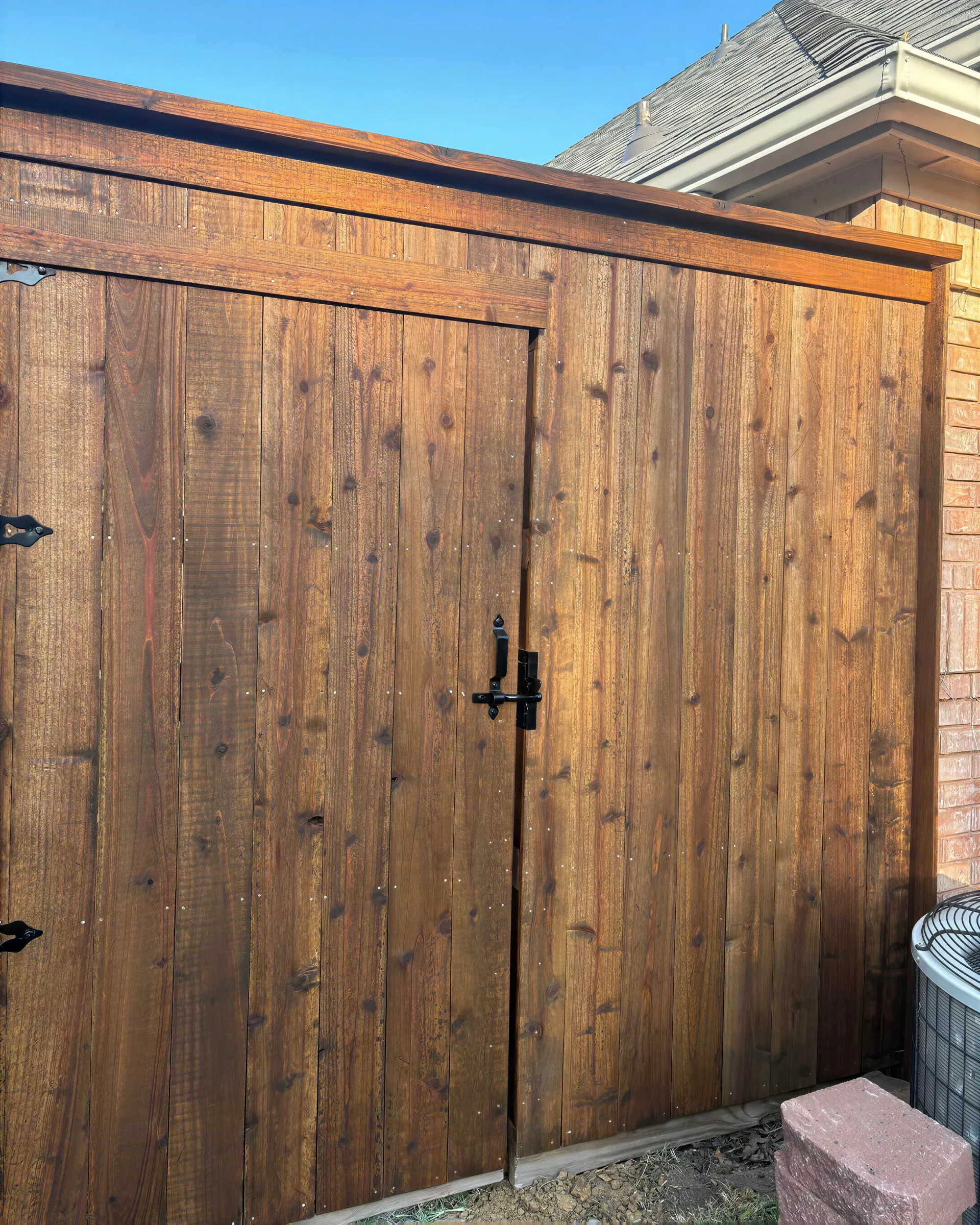 Wooden double gate with black handles and hinges beside a brick house wall.
