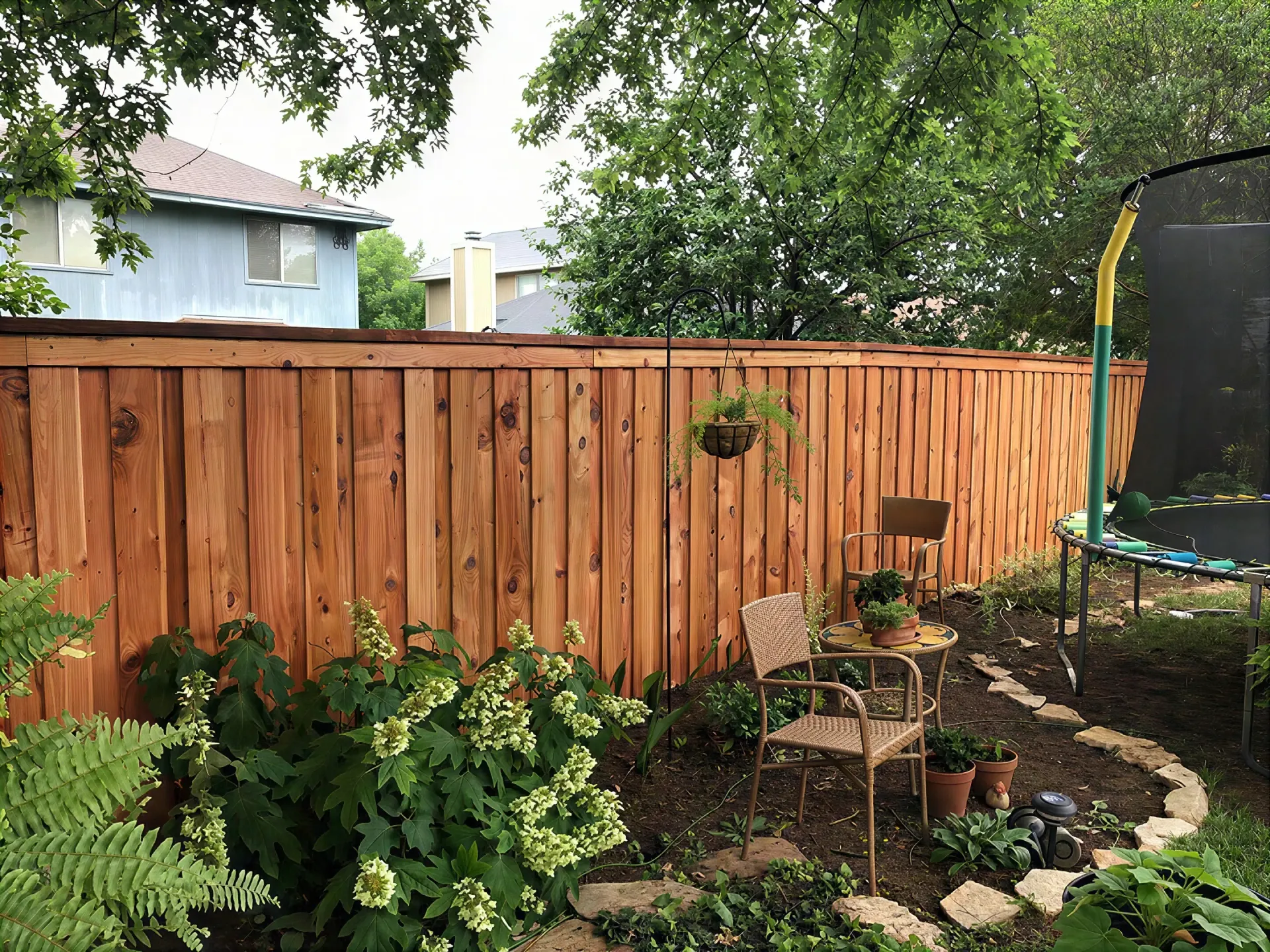 Backyard garden with wooden fence, leafy plants, and a trampoline on the right