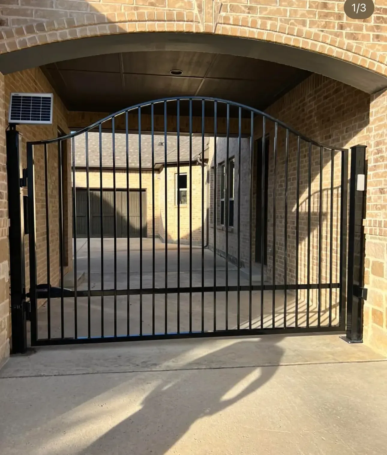 Black metal gate under a brick archway blocking entry to a courtyard or driveway.