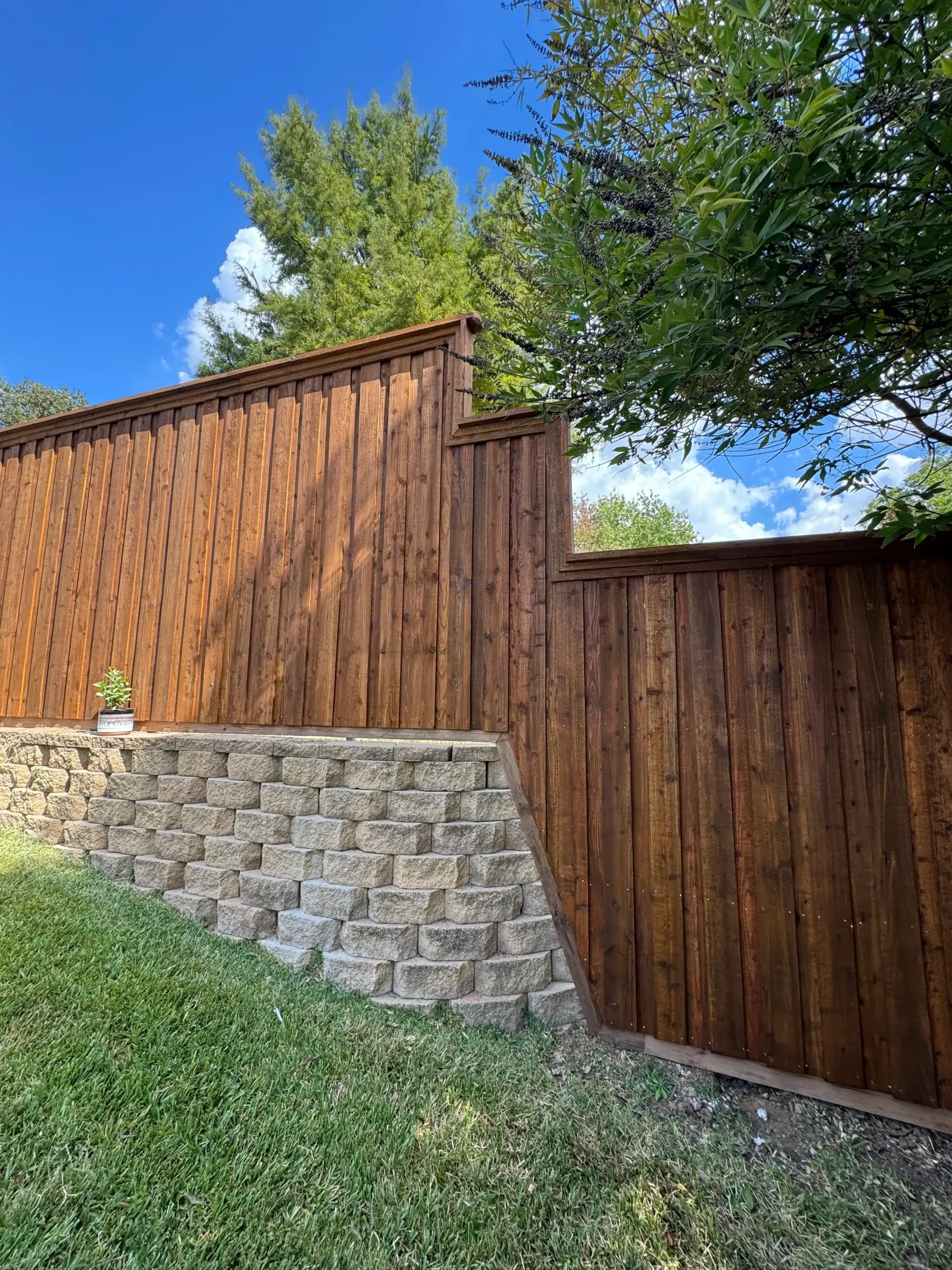 Wooden fence and stone retaining wall on a grassy slope under a blue sky.