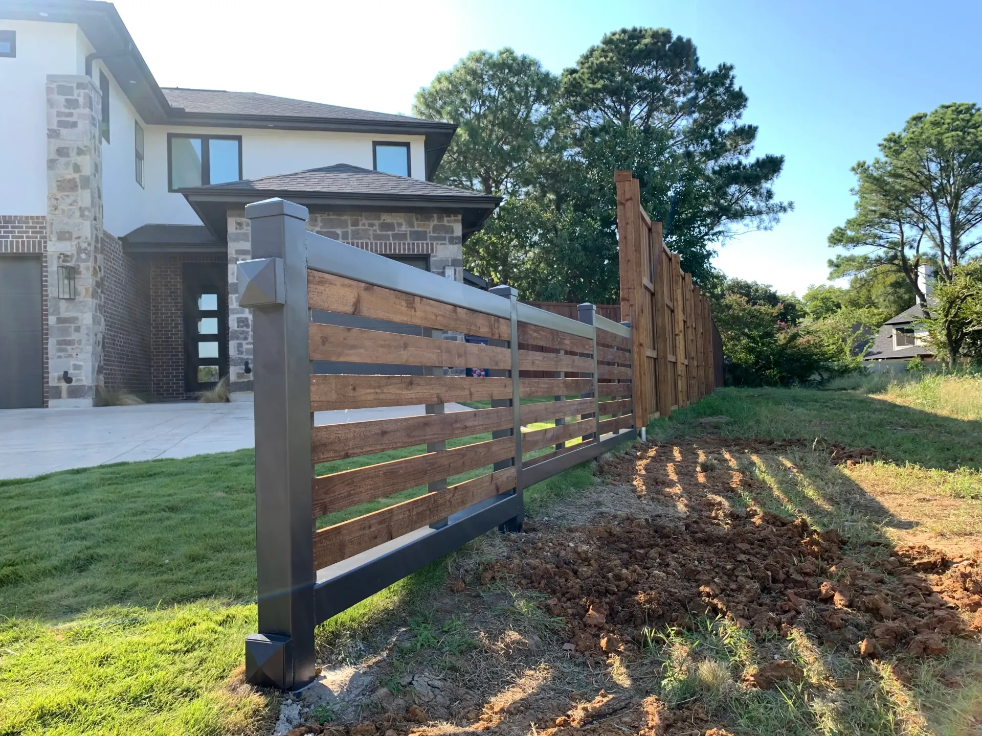 Modern home with a dark wood and metal fence along a grassy side yard