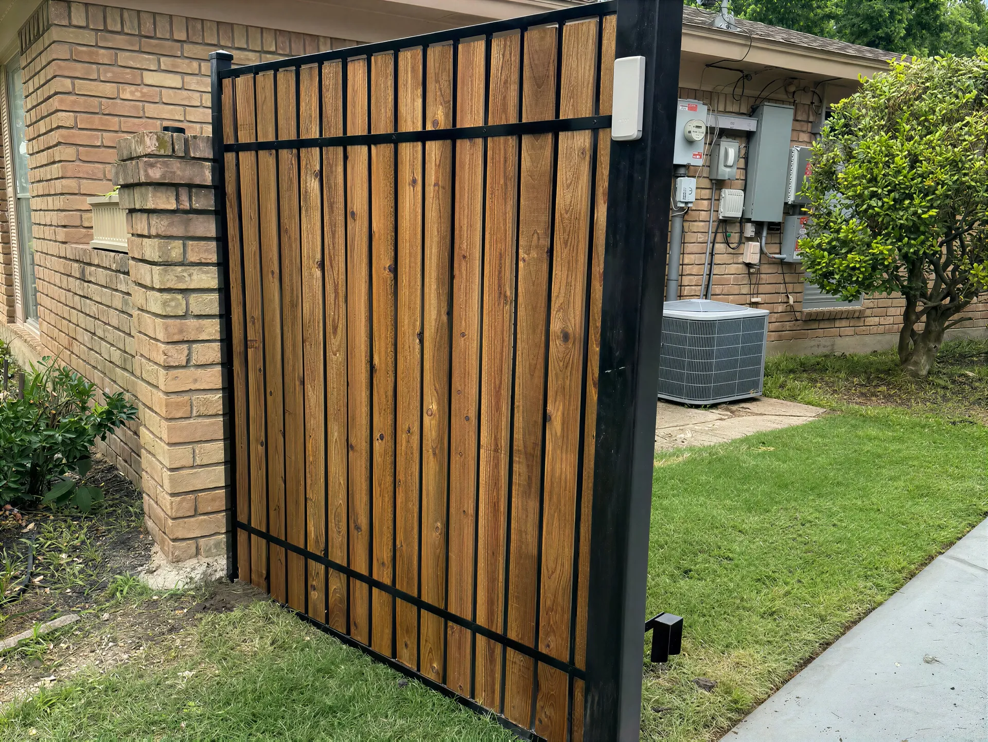Wooden side gate with black metal frame beside a brick house and sidewalk