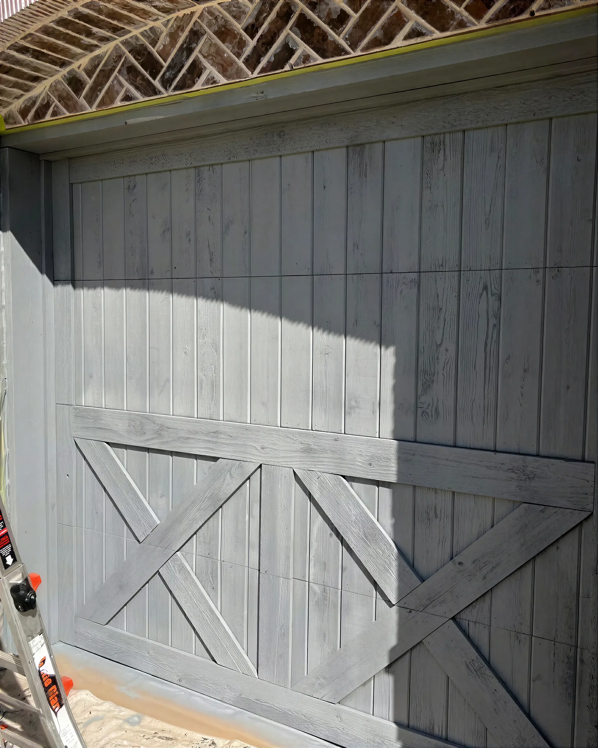 Weathered white barn door with diagonal wood trim in bright sunlight and shadow