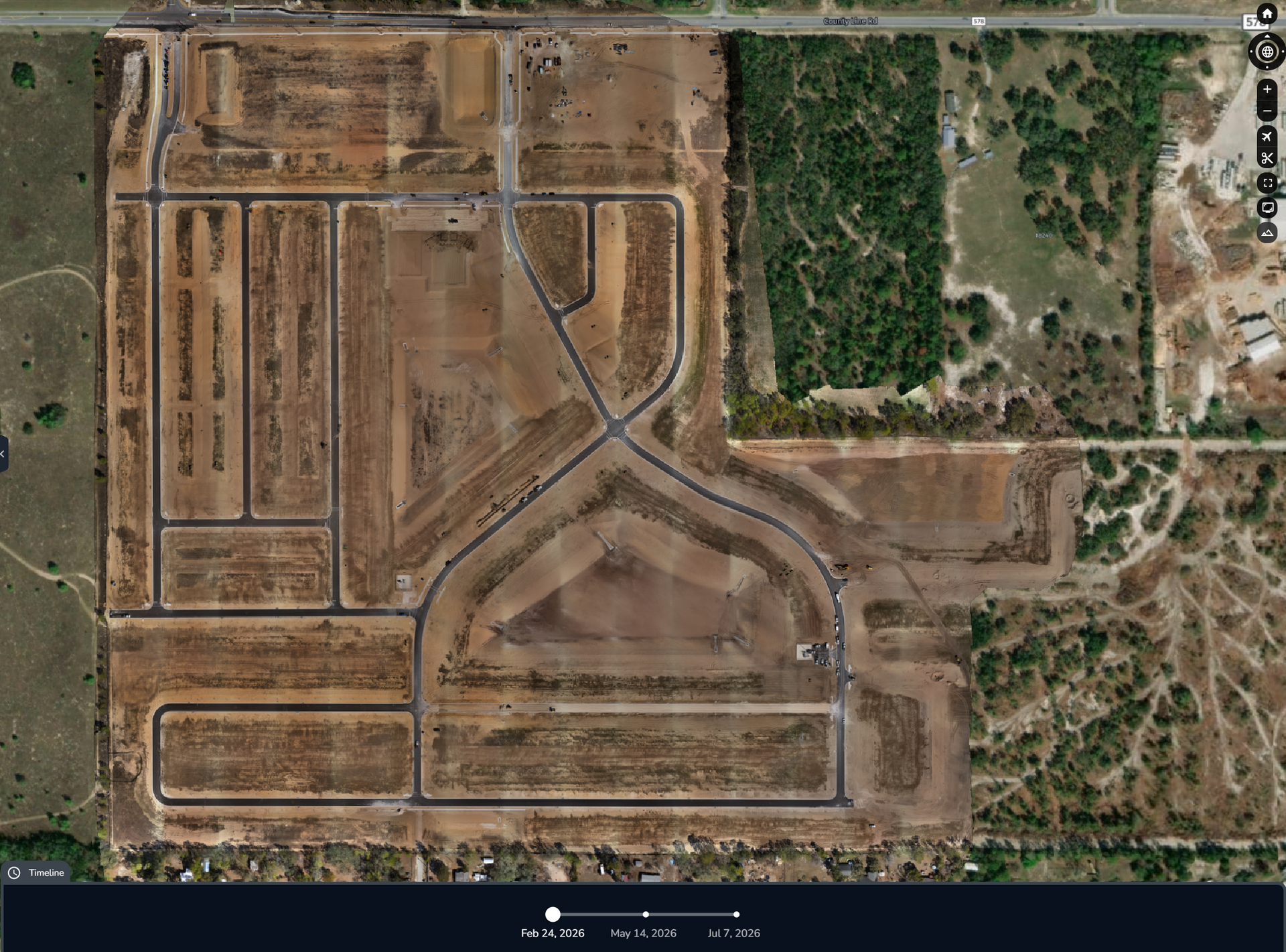 Aerial view of a dirt road subdivision with empty lots, green patches, and sparse buildings.