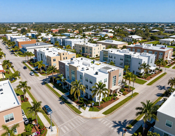 Aerial view of a sunny coastal neighborhood with white apartment buildings, palm trees, and intersecting streets.
