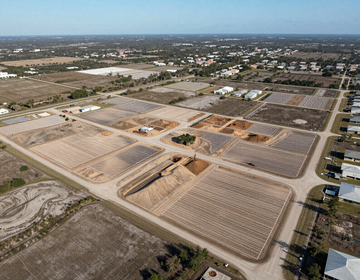 Aerial view of a large agricultural field with rectangular plots and surrounding farmland homes
