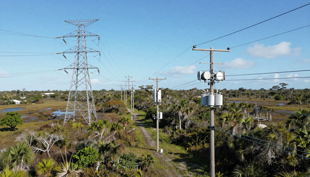 Rural utility corridor with power lines, poles, and transformers under a clear blue sky