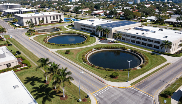 Aerial view of a modern office complex with two round ponds, a road, and palm trees