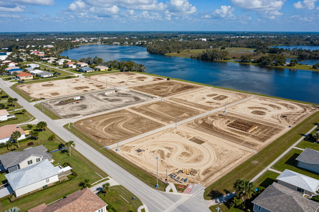 Aerial view of a large construction site beside a river, with paved roads and homes nearby.