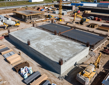 Construction site with large concrete foundation slabs, steel rebar, and yellow cranes under construction.