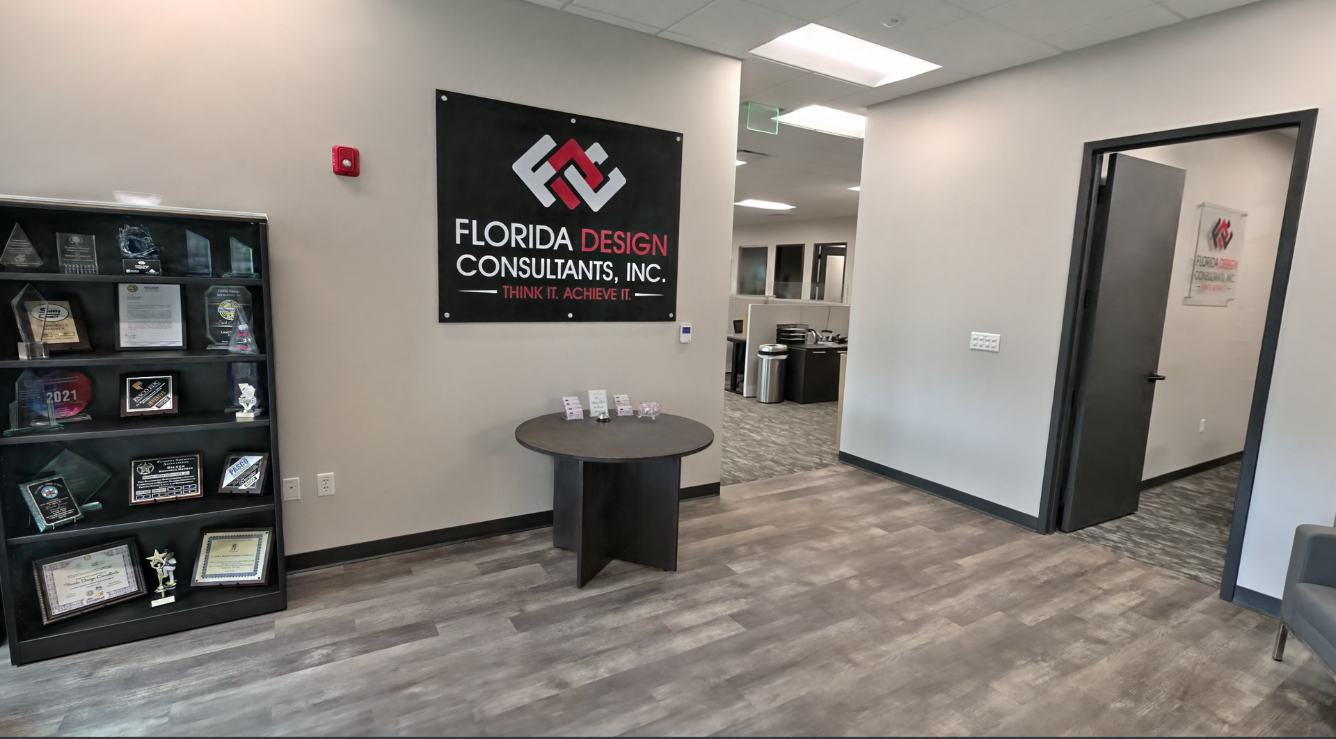 Office lobby with gray floors, round table, wall logo sign, and open doorway to a hallway