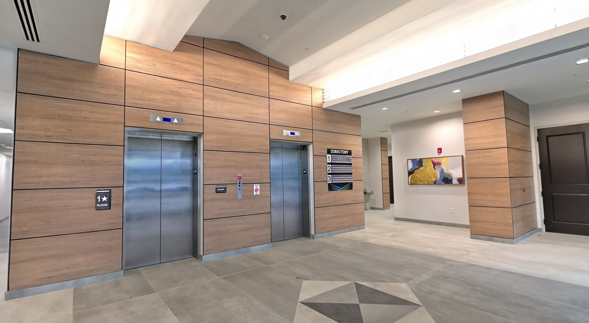 Modern lobby with two stainless steel elevators, wood-paneled walls, and tiled flooring.