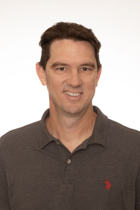 Portrait of a smiling man in a brown collared shirt on a plain white background