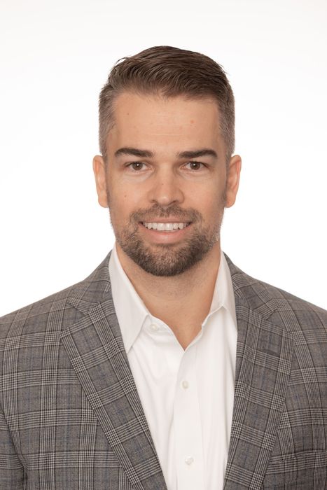 Studio headshot of a smiling man in a gray blazer and white shirt on a white background