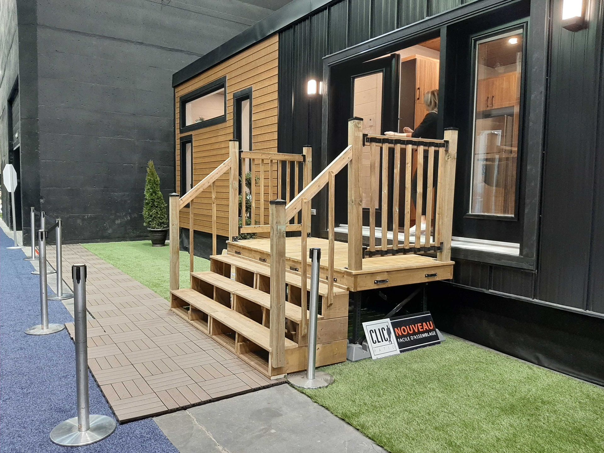 Extérieur d'une minuscule maison avec marches et rambarde en bois, bardage noir et petite pelouse.
