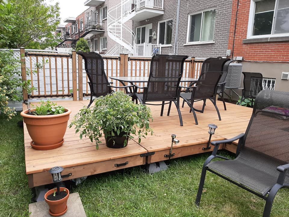Terrasse en bois avec mobilier de jardin dans un jardin. Des plantes en pot sont disposées sur la terrasse et dans le jardin.