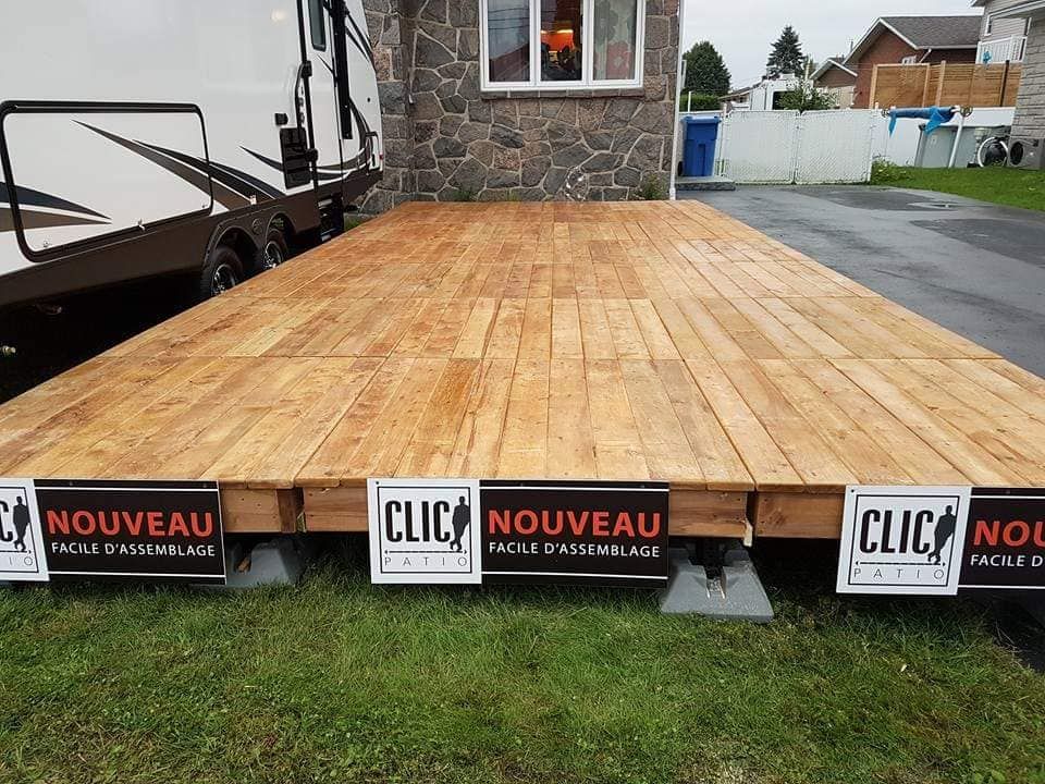 Terrasse en bois sur parpaings à côté d'une maison et d'un camping-car avec des banderoles publicitaires.