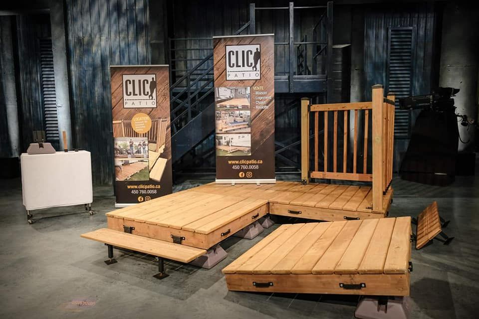 Système de pont CLIC Cabin présenté sur une scène, comprenant des plateformes en bois, une rambarde et des bannières publicitaires.