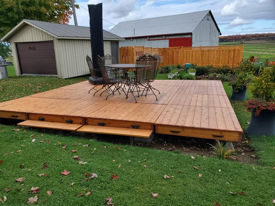 Terrasse en bois avec mobilier de jardin, abri de jardin et grange dans une cour gazonnée.
