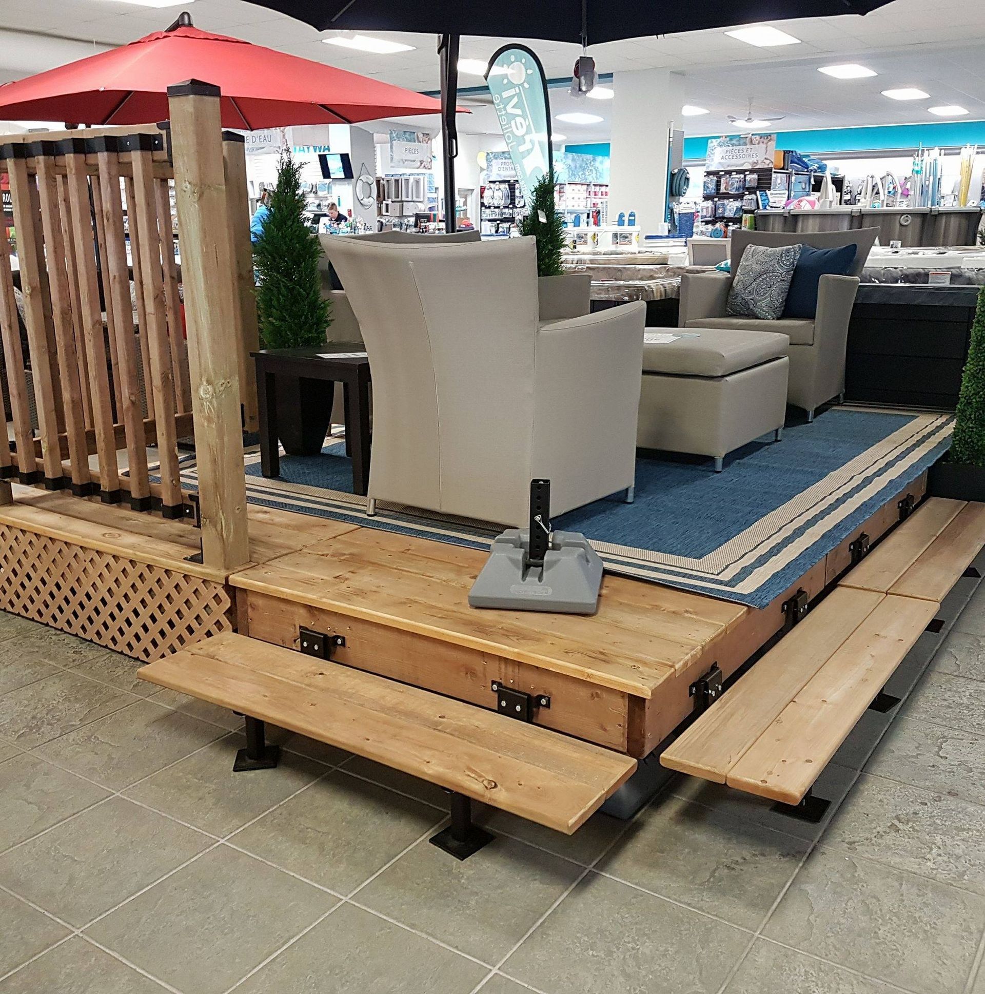 Mobilier d'extérieur exposé sur une terrasse en bois surélevée, avec parasol et treillis, à l'intérieur d'un magasin.