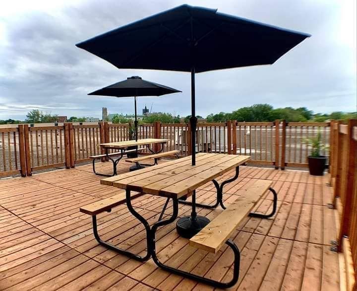 Terrasse extérieure avec tables de pique-nique, parasols noirs et terrasse en bois.