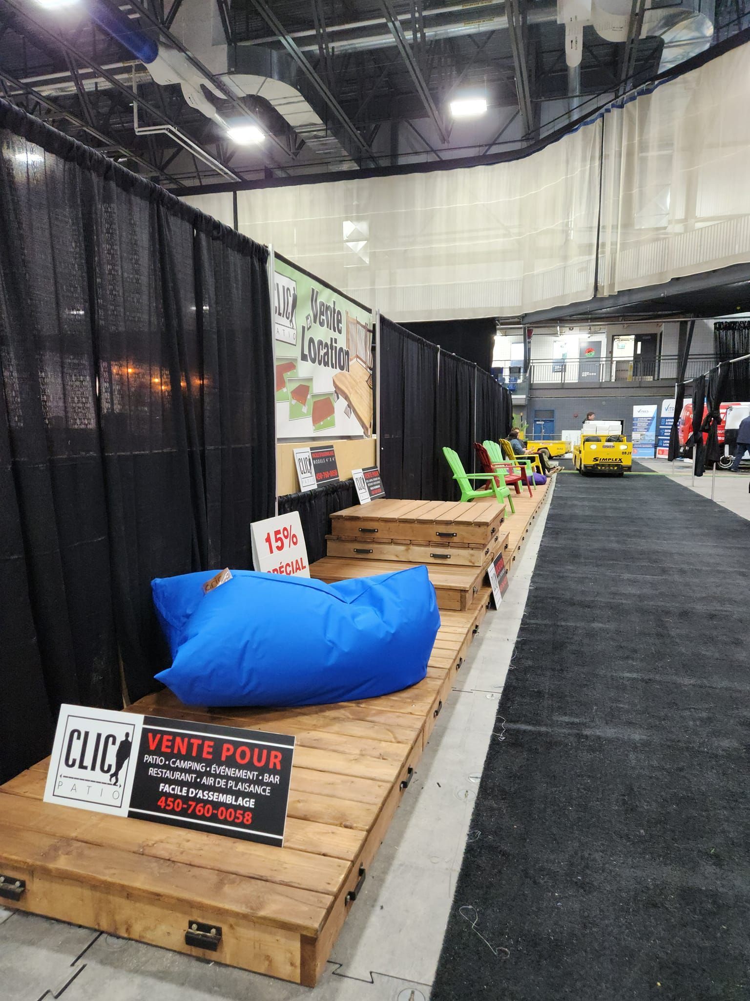 Stand d'exposition avec un pouf bleu, une estrade en bois et des rideaux noirs.