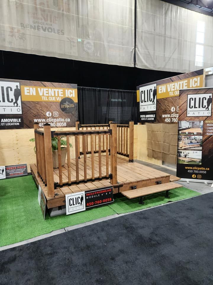Une terrasse en bois avec rambardes et marches lors d'un salon professionnel ; les panneaux indiquent « CLIC » et « EN VENTE ICI ».