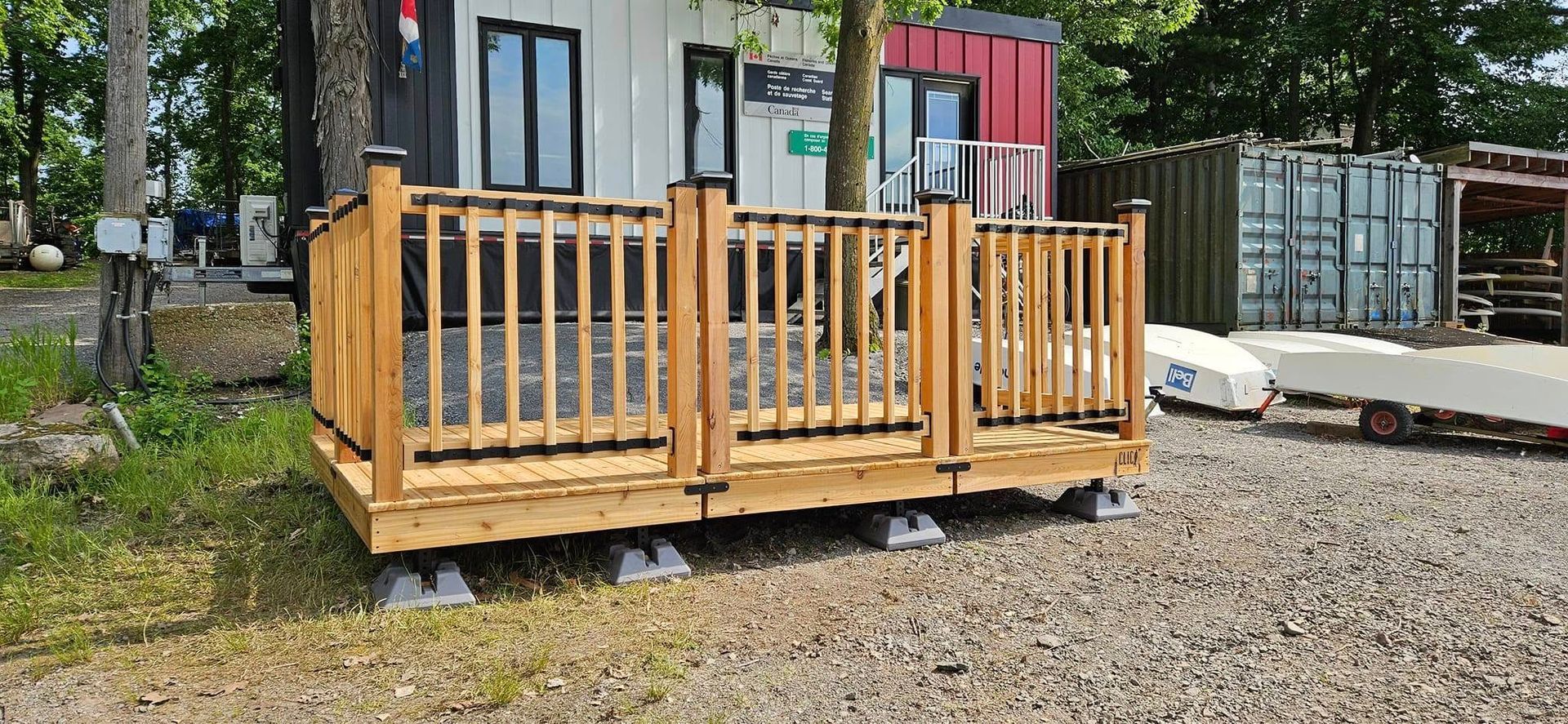 Terrasse en bois avec rambarde sur gravier, devant un bâtiment blanc aux finitions noires.
