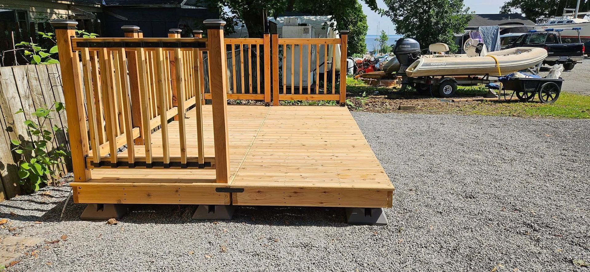 Terrasse en bois avec rambarde, posée sur du gravier, avec des bateaux en arrière-plan.