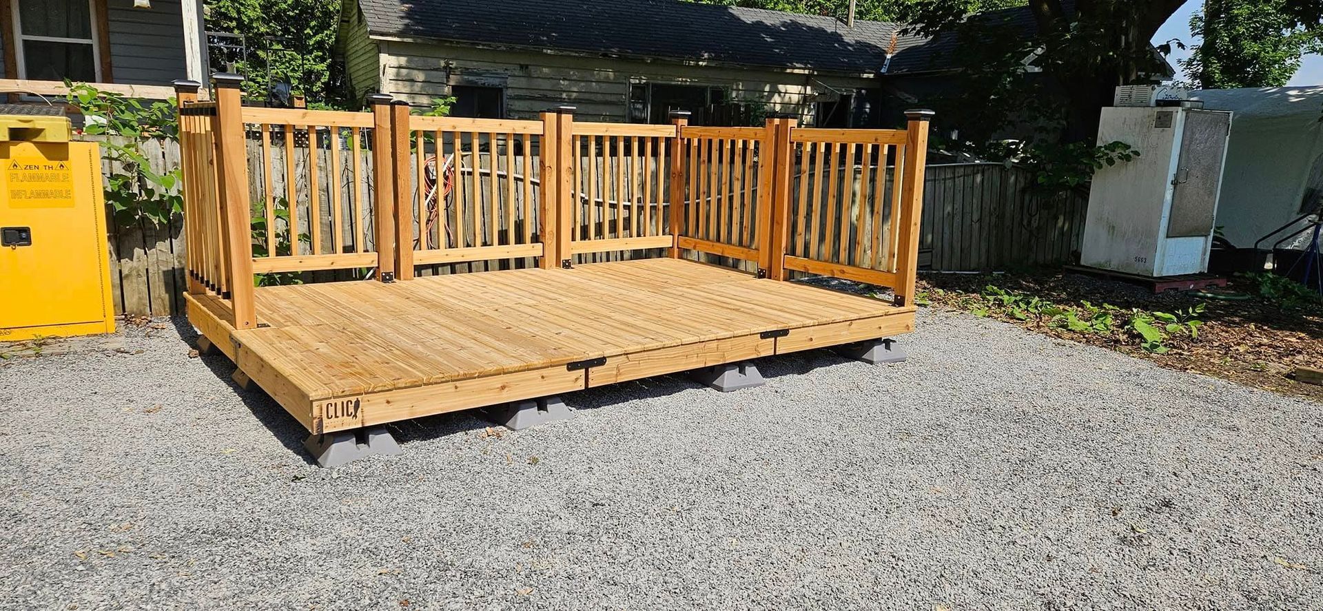 Terrasse en bois avec rambarde sur un sol gravillonné.