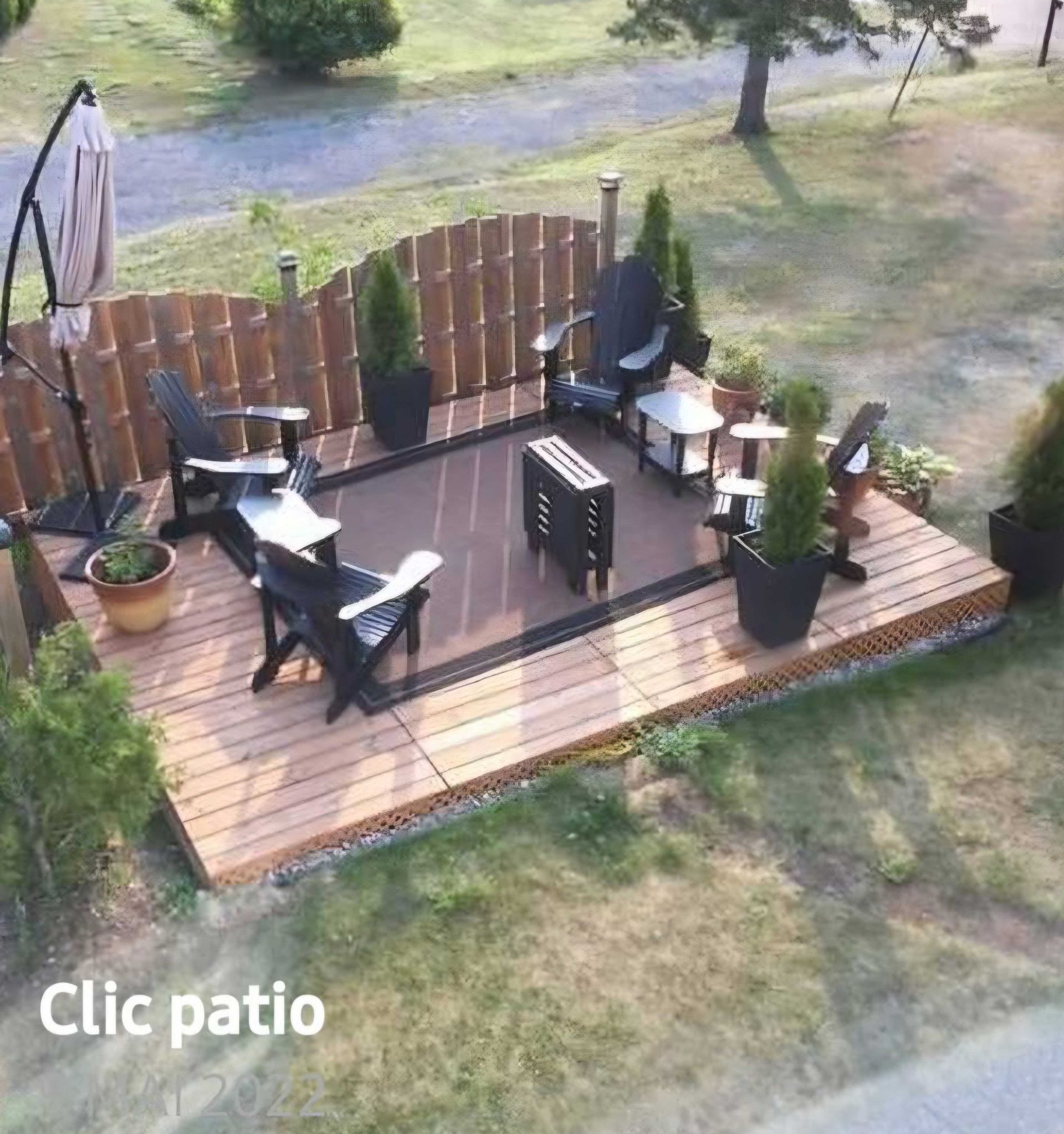 Patio avec terrasse en bois, chaises, table, parasol et plantes décoratives, le tout entouré d'une clôture.