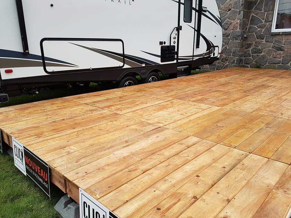 Plateforme en bois devant une caravane. Le plancher est constitué de planches.