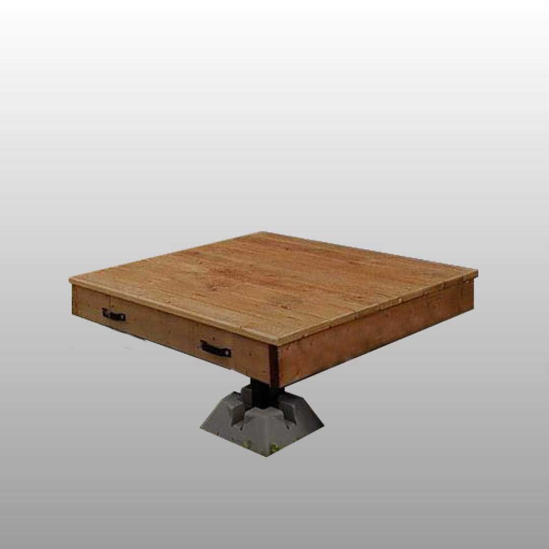 Table carrée en bois avec poignées de tiroir, montée sur un piédestal gris.
